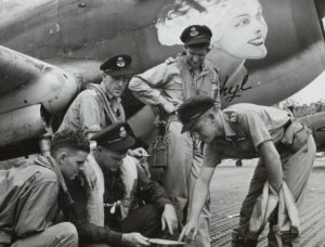 "a group of 77 squadron pilots posed next to a P-40 Kittyhawk aircraft"